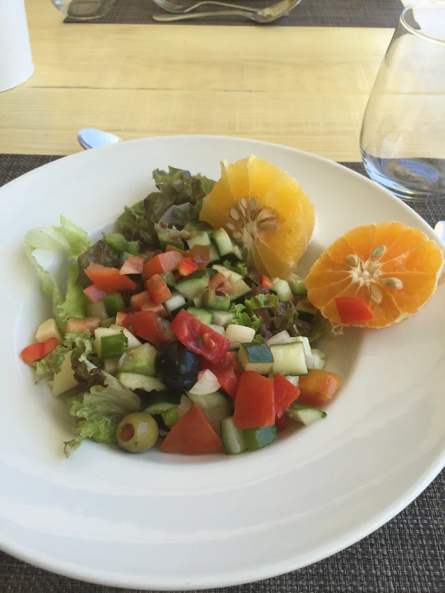 A restaurant salad of chopped tomato, cucumber, pepper and olive on lettuce, served with two halved oranges