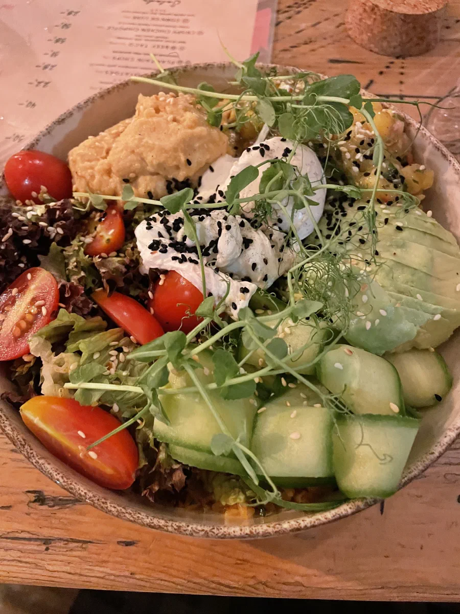 A restaurant salad bowl topped with pea shoots, with cherry tomatoes, sliced cucumber, avocado and salad leaves